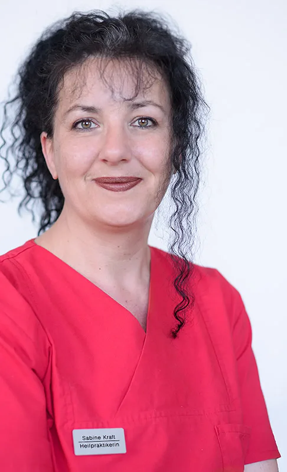 Sabine Kraft in roter Praxiskleidung, am Namensschild: Sabine Kraft, Heilpraktikerin
